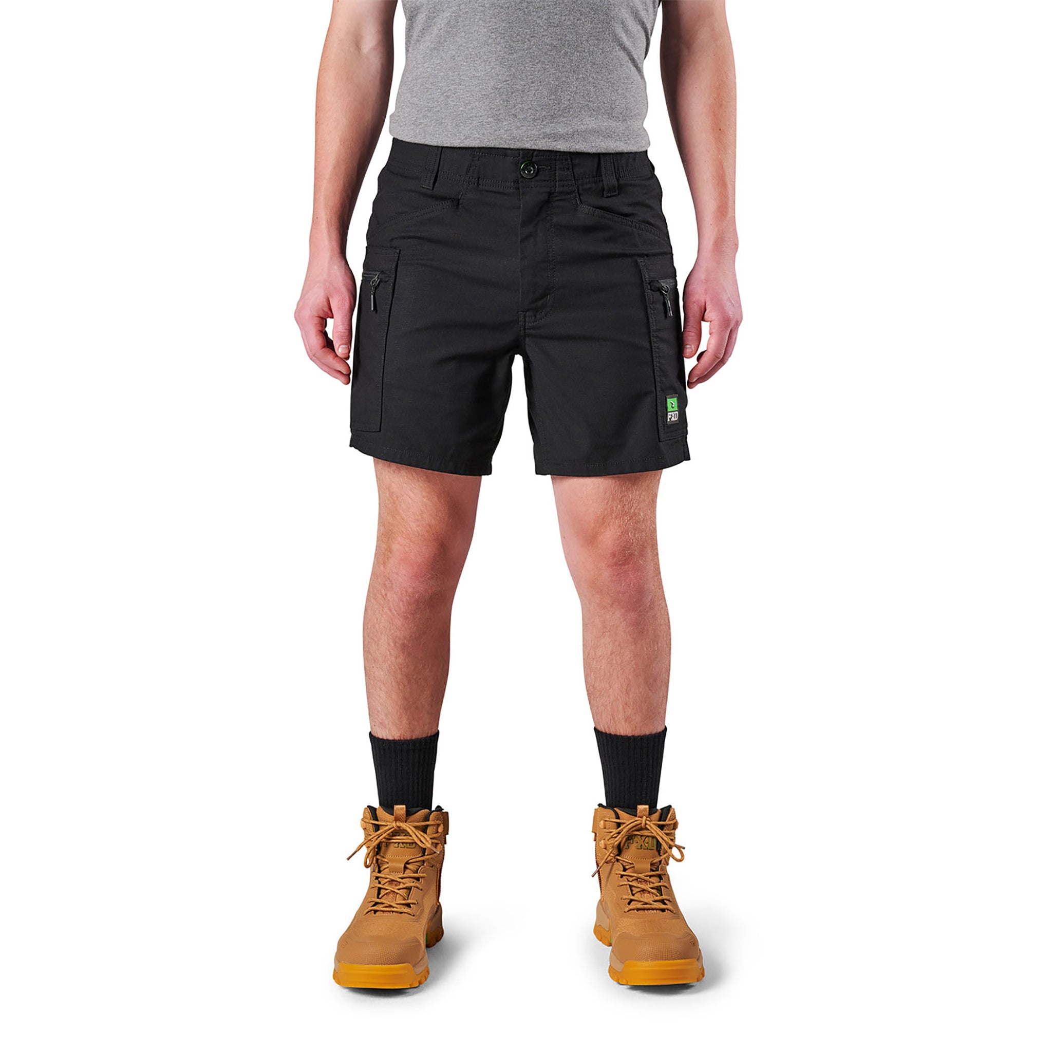 A person standing against a white background, wearing black FXD cargo shorts and brown boots.